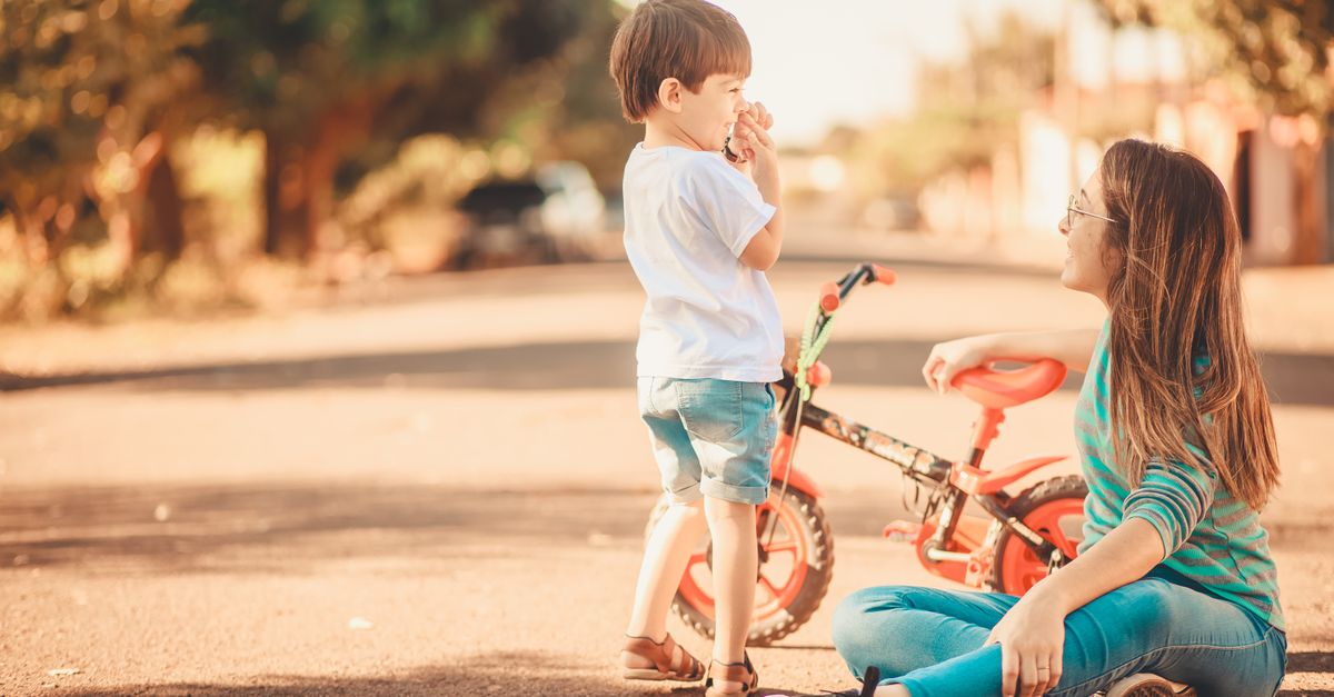 Mãe sentada na calçada conversando com o filho pequeno, em um dia ensolarado