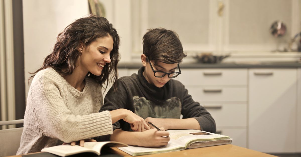 Jovem sorridente ajudando o irmão mais novo com a lição de casa, sentados à mesa com livros