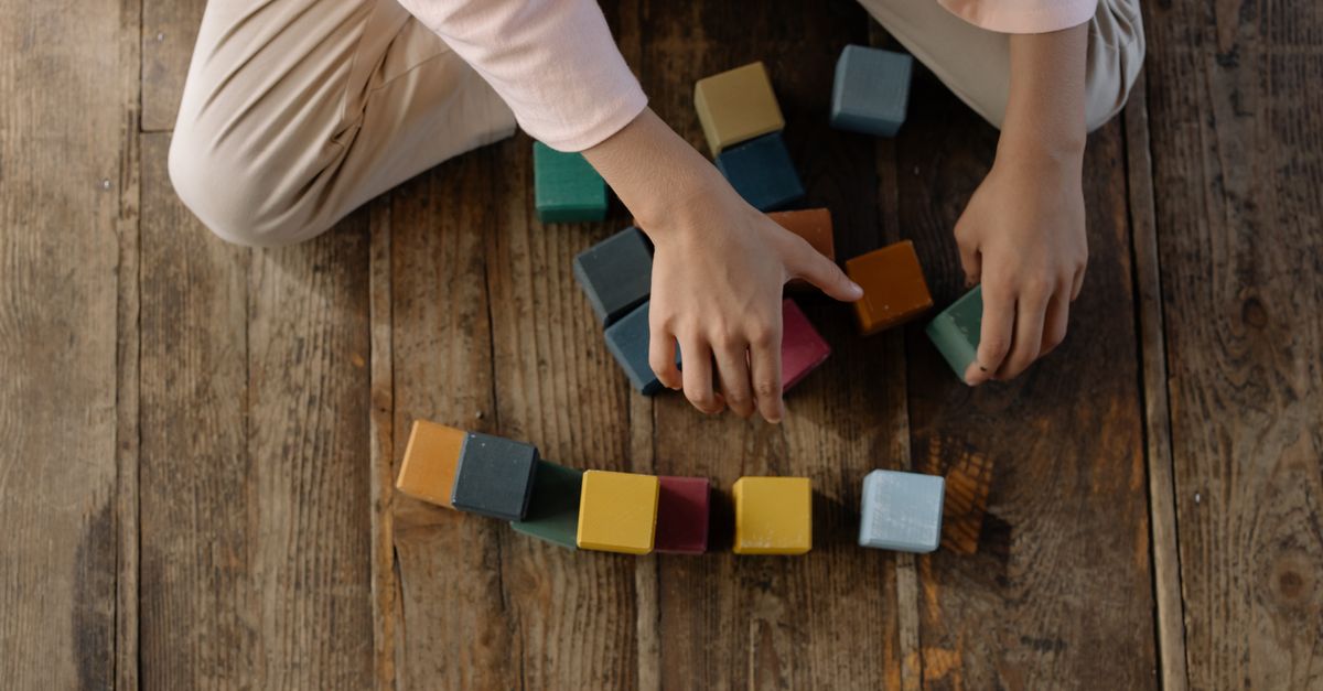 Criança organizando blocos de brinquedo coloridos no chão de madeira